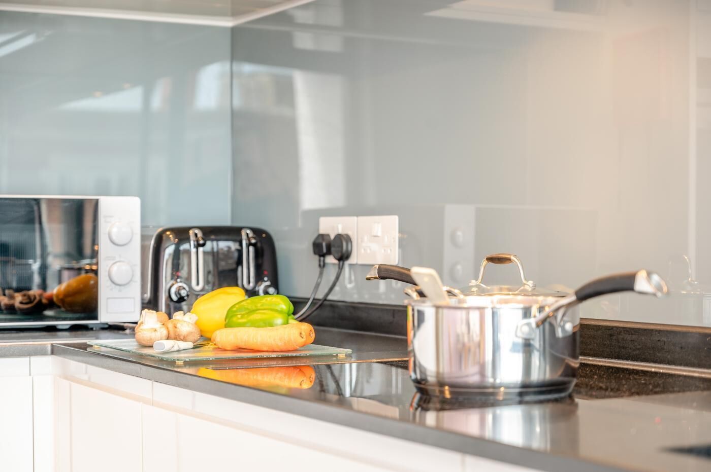 A modern kitchen with a toaster, a cutting board with vegetables, and a pot on the counter.