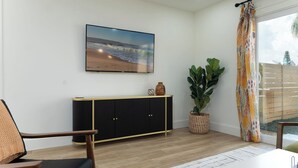 Un salon moderne doté d’un grand téléviseur à écran plat, d’un meuble noir et doré, d’une grande plante et offrant une vue sur l’extérieur.