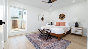 Une chambre à coucher comprenant un lit, une table de chevet, une lampe, un ventilateur de plafond, une fenêtre et une porte.