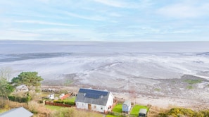 Eine Küstenlandschaft mit einem Haus, einem kleinen Garten und Blick aufs Meer.
