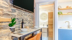 A dining area with a stone wall, a flat-screen TV, a table set with plates, a bottle, and a plant. - 2 Bed in Lynton (oc-v42649) (Lynmouth)