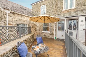 A stone house with a patio, a table with chairs, and a covered area with an umbrella. - 2 Bed in Lynton (oc-v42649) (Lynmouth)