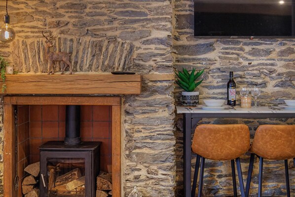 A stone wall interior with a fireplace, a mounted TV, and a dining area with chairs and a table. - 2 Bed in Lynton (oc-v42649) (Lynmouth)