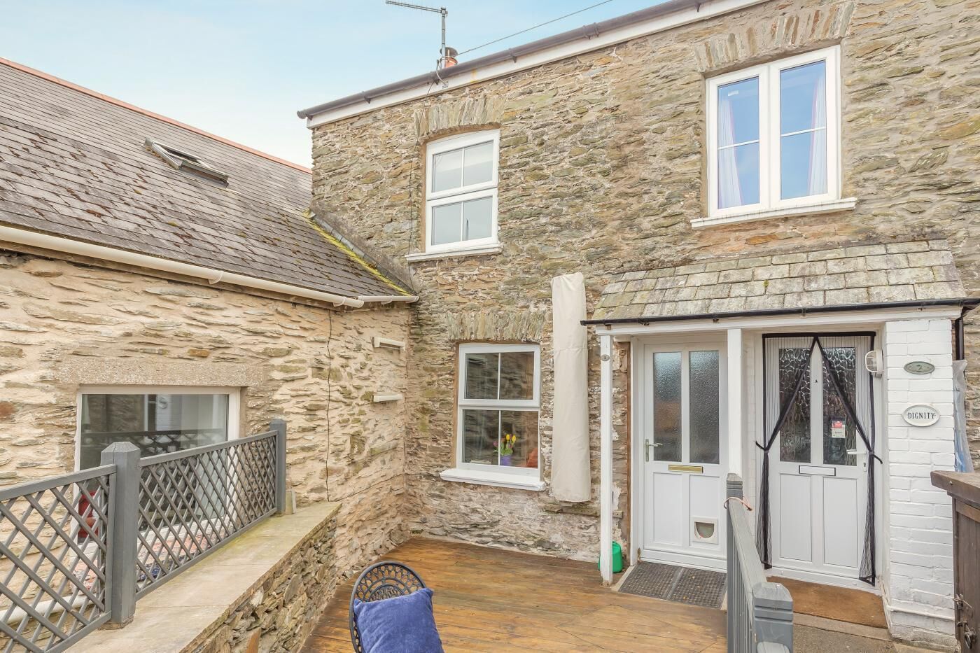 Un bâtiment en pierre avec une porte blanche, un petit balcon et une terrasse en bois.