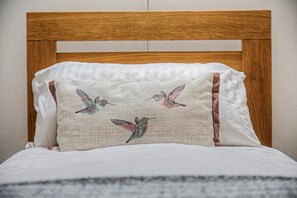 Ein Bett mit einem hölzernen Kopfteil und einem Kissen mit aufgestickten Kolibrige.