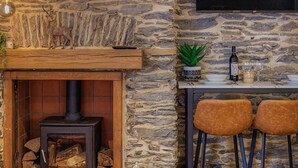 A stone wall interior with a fireplace, a mounted TV, and a dining area with chairs and a table. - 2 Bed in Lynton (oc-v42649) (Lynmouth)