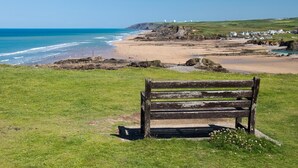 A bench overlooking a beach with a clear view of the ocean and distant hills.