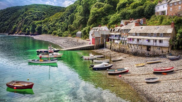 A coastal village with boats docked along the shore, stone buildings, and a rocky beach.