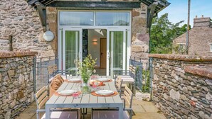 Ein Steingebäude mit einem Patio, an dem ein Esstisch gedeckt ist, einem Glastür-Eingang und einer Mauer aus Stein, die den Patio umgibt.