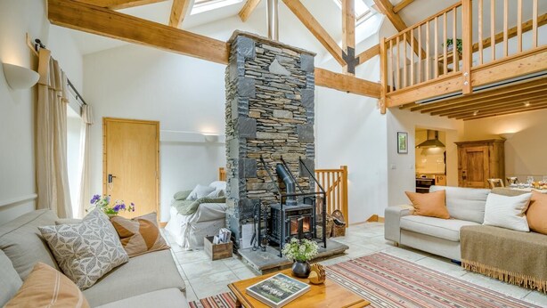A cozy living room with a stone fireplace, wooden beams, and a high ceiling.