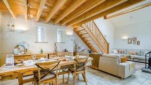 A spacious living area with a wooden dining table, chairs, a sofa, and a staircase.