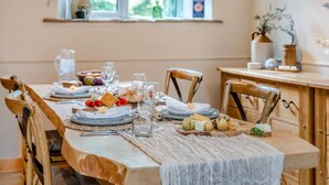 A dining table set with plates, glasses, and a variety of food items, with wooden chairs and a window in the background.