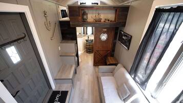 Un intérieur compact comprenant un canapé, une étagère en bois agrémentée d’objets décoratifs, une porte avec une poignée et une fenêtre avec des rideaux.