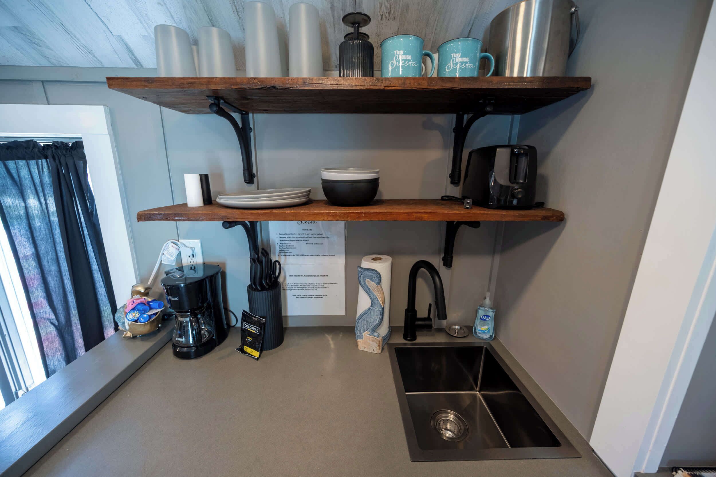 A kitchen with a coffee maker, a sink, and shelves with dishes and mugs.