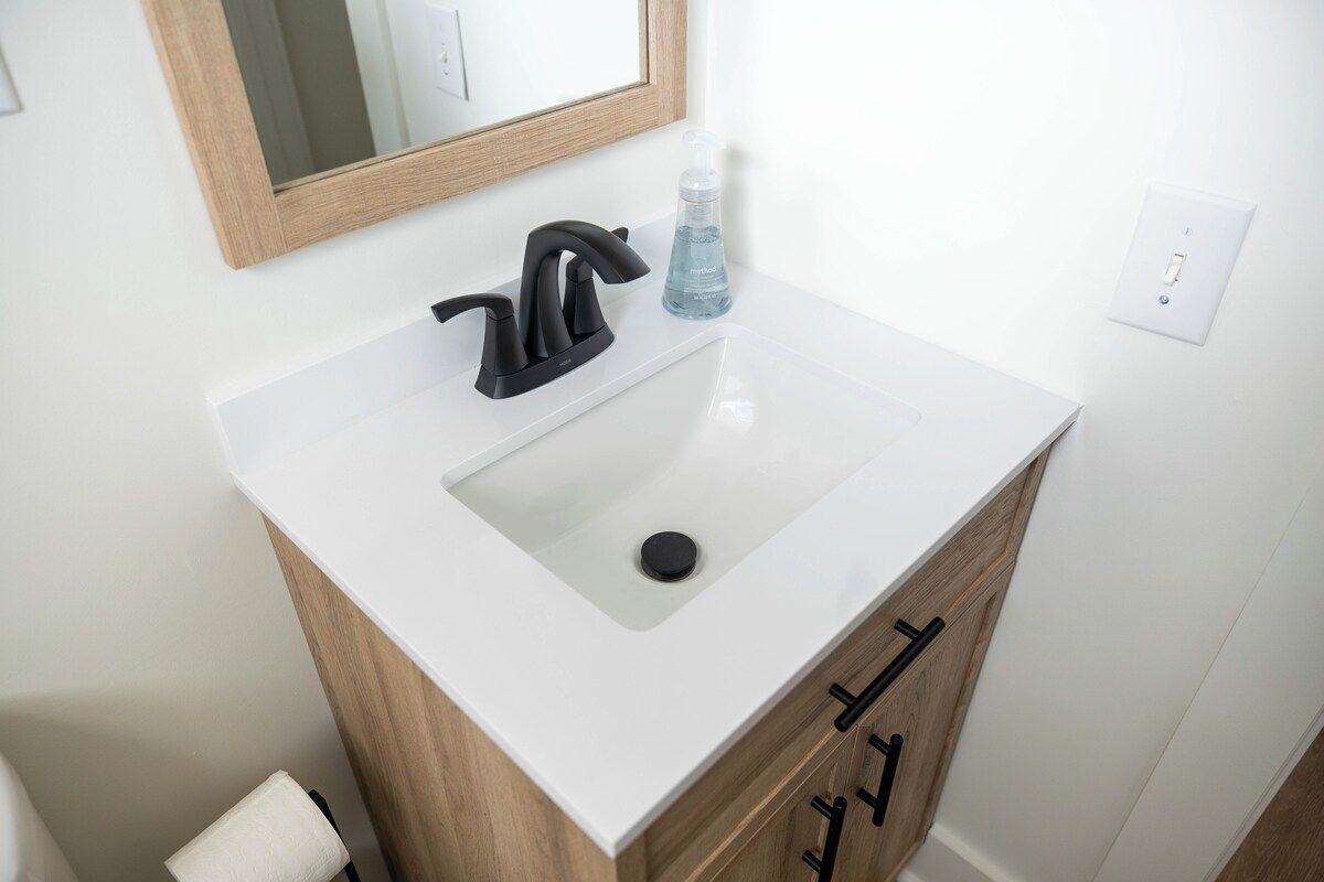 Une salle de bain avec un lavabo blanc, un robinet noir, un meuble en bois et un miroir.