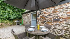 A round outdoor table with wicker chairs, a large umbrella, and a stone wall in the background. - 2 Bed in Duloe (oc-r27525) (Duloe)