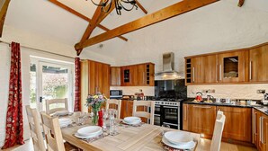 A kitchen with wooden cabinets, a dining table set for four, and a large stove. - 3 Bed in Duloe (oc-h27526) (Duloe)