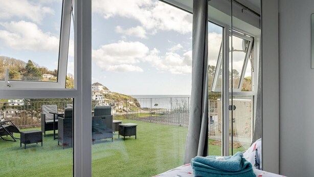 Un balcón con vista al mar, una cama con colcha estampada y una ventana con vista al mar y edificios.