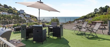 Un patio al aire libre con una parrilla, mesa de comedor, sillas y un paraguas grande.