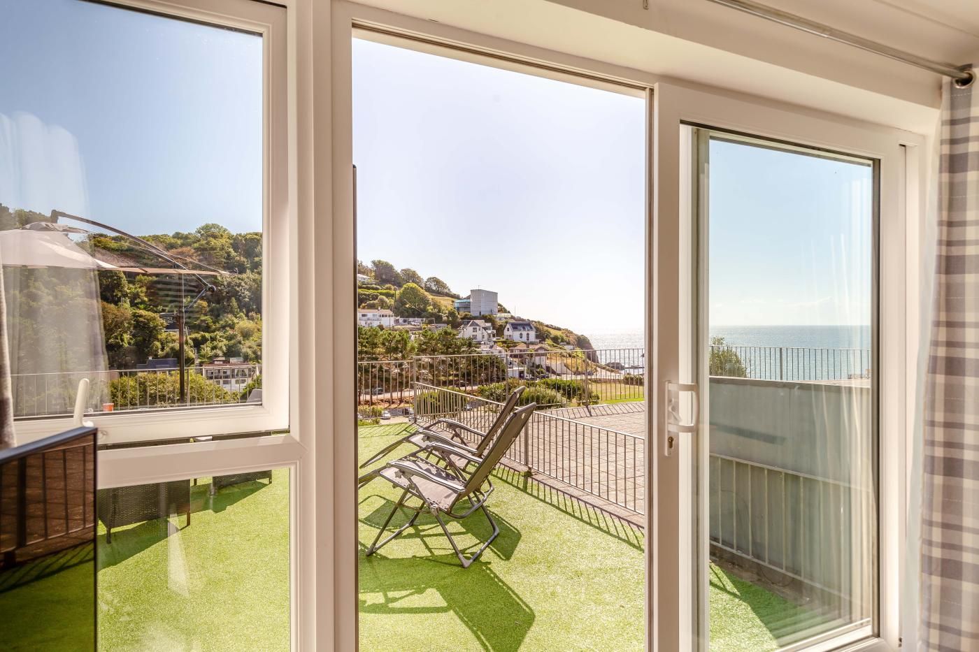 A balcony with a view of a coastal town, a chair, and a glass door.