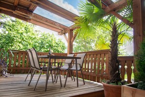 Une terrasse en bois avec une table et des chaises, entourée d’une clôture en bois et d’une végétation luxuriante.