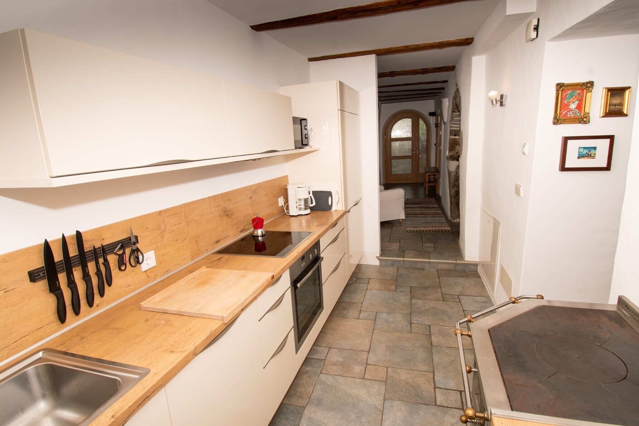 A kitchen with a wooden countertop, a sink, and a stove. There is a hallway leading to another room.
