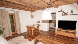 A living room with a wooden ceiling, a dining area with a table and chairs, a TV on a wooden stand, and a chandelier. - Saxöler – Cozy Apartment in Historic Winery near Brixen (Brixen)