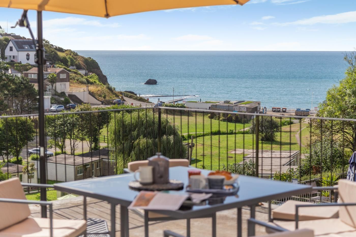 A balcony with a table, chairs, and a view of the sea and houses.