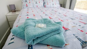 Un lit bien fait, avec une couvre-lit à motifs, une couverture turquoise et un oreiller portant une étiquette indiquant qu’il provient d’un spa.
