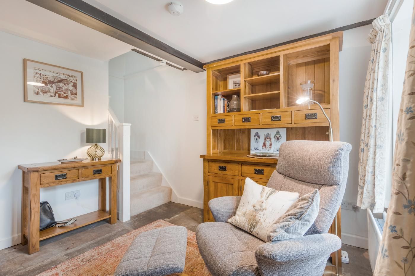 A cozy living room with a wooden cabinet, a comfortable armchair, a small desk, and a staircase.