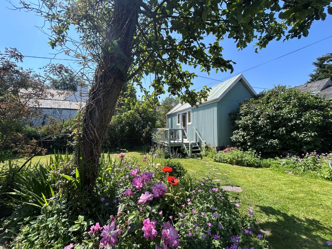 Ein Haus mit einer Veranda, umgeben von einem Garten mit verschiedenen Pflanzen und Blumen.