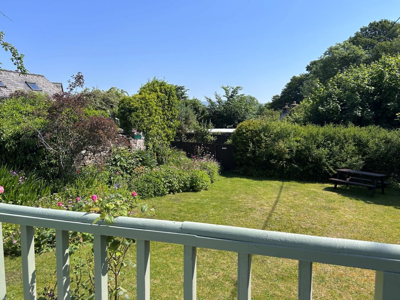 A well-maintained garden with a lawn, a wooden bench, and a variety of plants and trees.