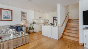 Een moderne woonkamer met een bank, salontafel en een keukenhoek met witte kasten en een houten trap.