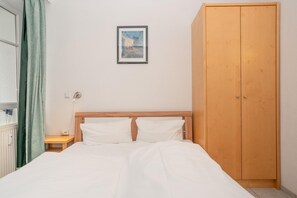 Ein Schlafzimmer mit einem Bett, einem Holzschrank, einem Nachttisch mit Lampe und einem gerahmten Bild an der Wand.