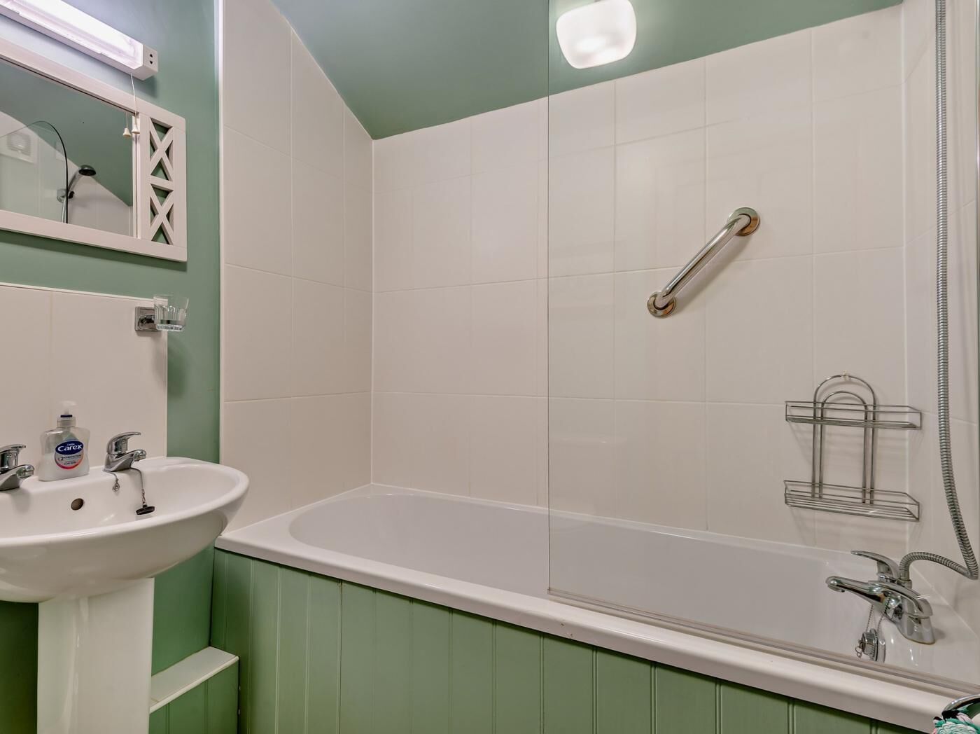 Une salle de bain avec un lavabo blanc, un miroir, une douchette à main et une baignoire.