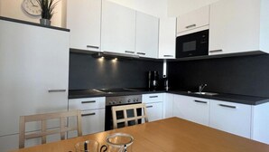 Uma cozinha moderna com armários brancos, bancada preta, fogão e micro-ondas.