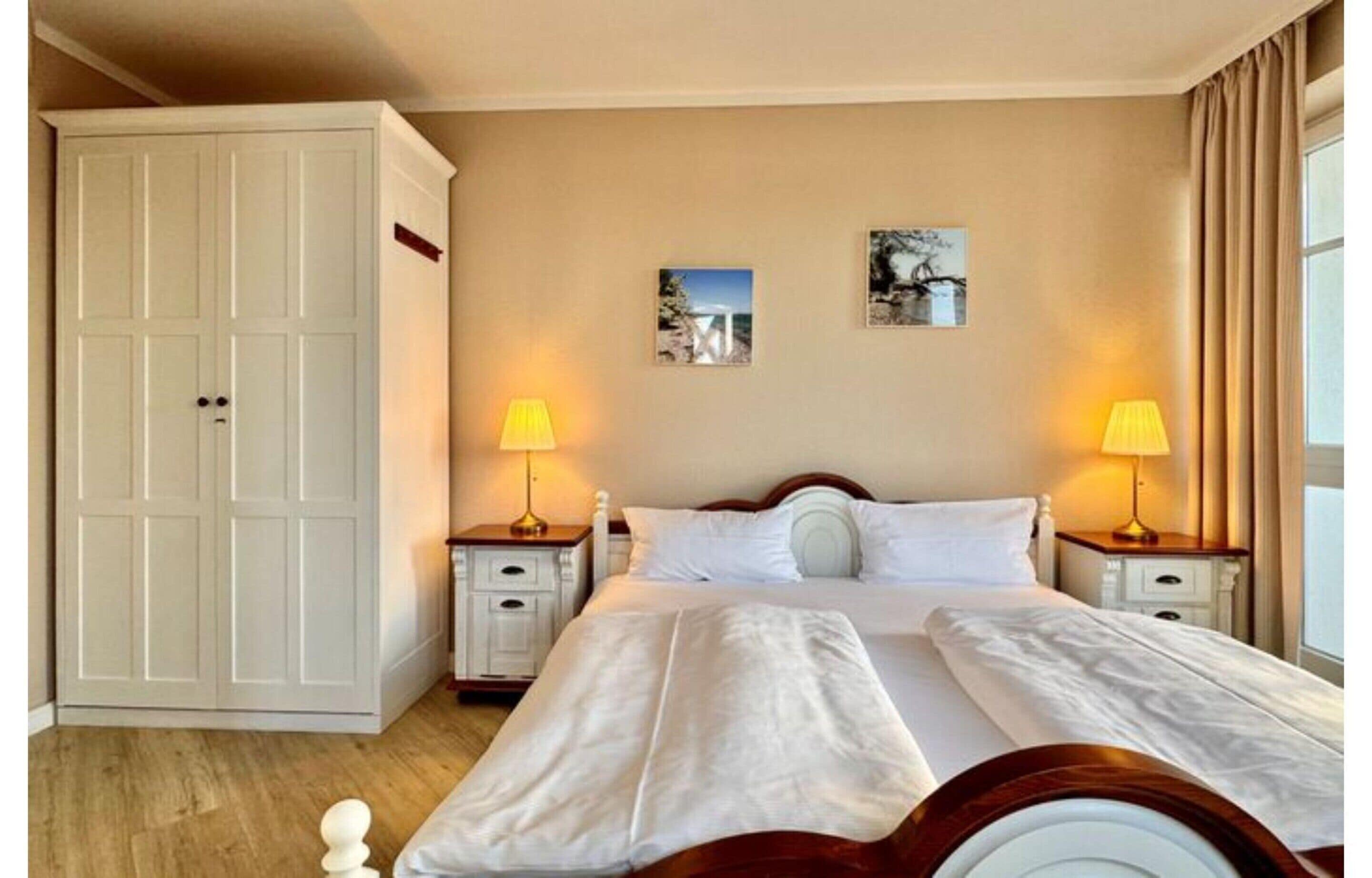A hotel room with a bed, two bedside tables, a wardrobe, and two wall-mounted lamps.