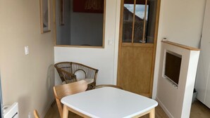 Una cocina compacta con una mesa blanca y sillas de madera, un ventanal pequeño y una puerta de madera.