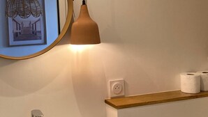 Un baño con un lavamanos blanco, un espejo, una lámpara colgante y un cuadro en la pared.