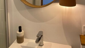 Un baño con un espejo redondo, un lavamanos, una llave, una botella de jabón y una lámpara colgante.