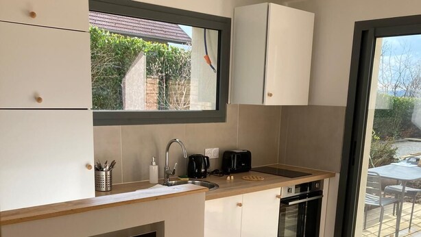 Una cocina moderna con armarios blancos, horno integrado, cafetera y ventana con vista a un jardín.