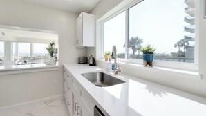 A modern kitchen with a large window, a stainless steel sink, and a white countertop. - Be a Nomad | Stunning Oceanfront 7-bedroom Home (Jacksonville Beach)