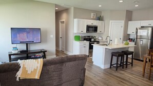 A modern kitchen with white cabinets, a central island with stools, a built-in microwave, and a stainless steel refrigerator. - New Construction Zero Entry in N Wichita (Wichita)