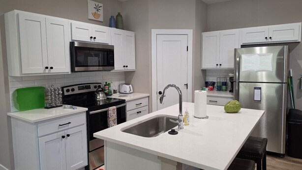 A modern kitchen with white cabinets, stainless steel appliances, and a central island with a sink. - New Construction Zero Entry in N Wichita (Wichita)