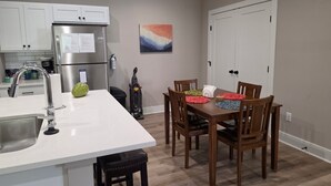A kitchen with white cabinets, a stainless steel refrigerator, a sink, and a dining area with wooden chairs and a table. - New Construction Zero Entry in N Wichita (Wichita)