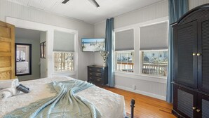 Quarto com cama, cómoda e janelas amplas com persianas.