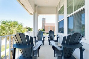 Ein Balkon mit vier Adirondack-Stühlen und einem Tisch, mit Blick auf ein Gebäude mit einem Turm.