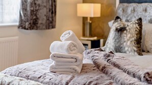 Un lit bien fait, avec une serviette blanche pliée, une couverture à motifs et un oreiller posé sur un mur à texture.