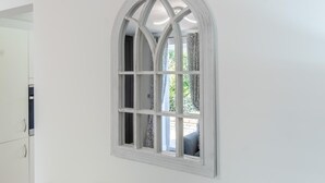 Uma janela arqueada branca com padrão quadriculado, uma parede branca e um vislumbre de um quarto com cortinas estampadas.