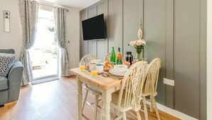 Uma sala de jantar com mesa de madeira, cadeiras, itens de café da manhã e uma TV de tela plana na parede.